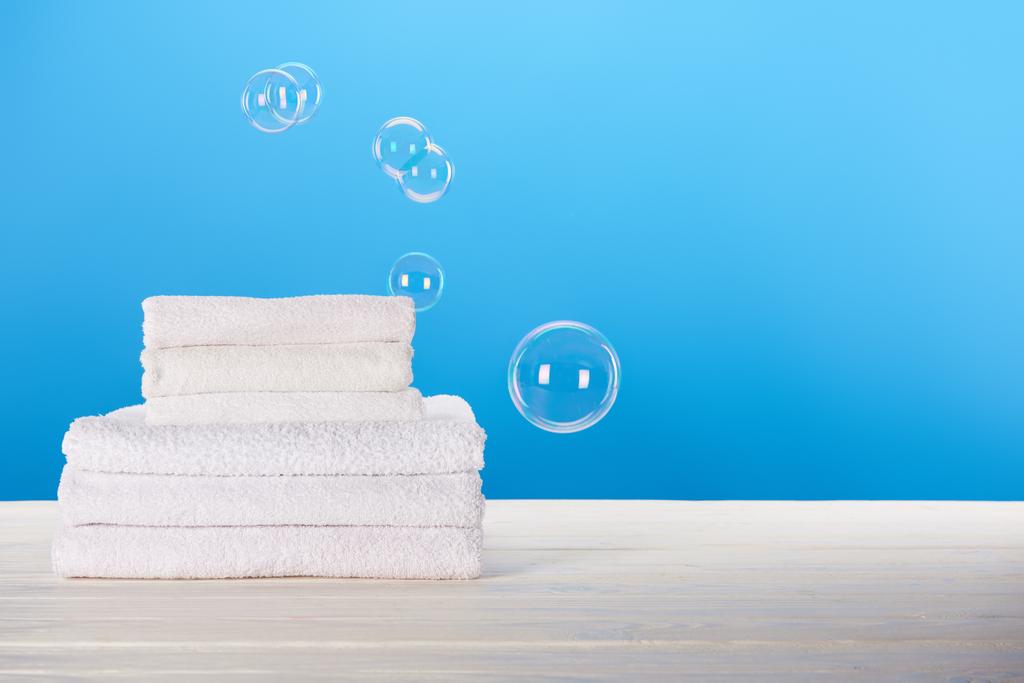 vista de cerca de toallas blancas limpias y burbujas de jabón sobre fondo azul
    - Foto, imagen