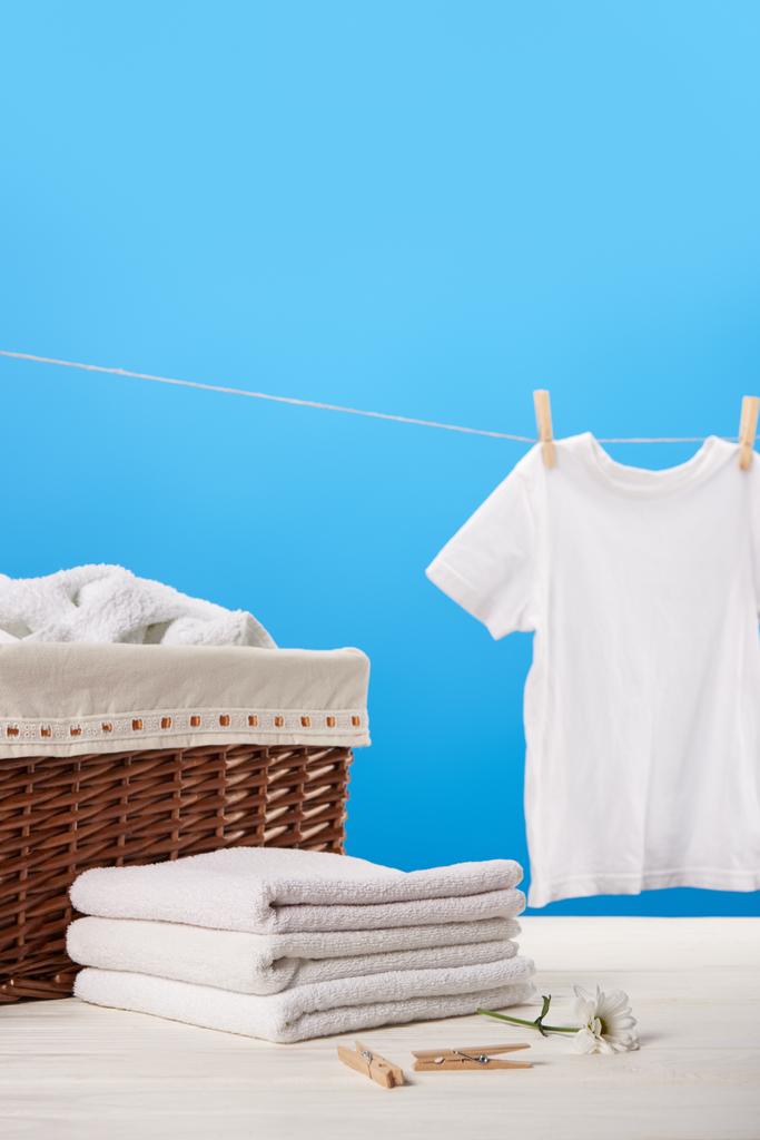 cesta de la ropa, pila de toallas limpias, pinzas de ropa, flor de manzanilla y camiseta blanca colgando en el tendedero en azul
 - Foto, imagen