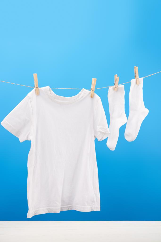 czysty, biały t-shirt i skarpetki wiszące na clothesline na niebiesko - Zdjęcie, obraz