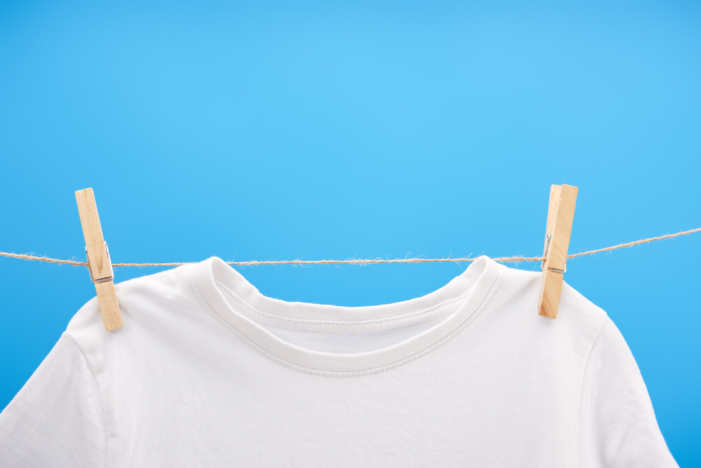 vista ravvicinata di t-shirt bianca pulita con mollette appese su corda isolata su blu
   - Foto, immagini
