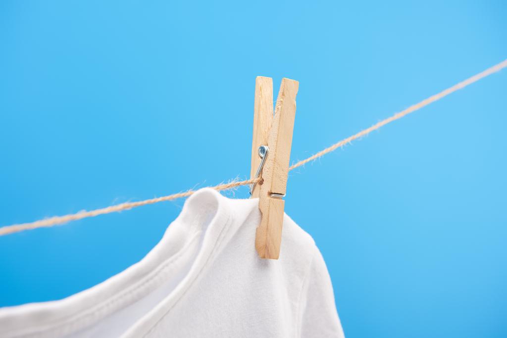 洗濯挟みの青に分離されたロープにぶら下がっているときれいな白い t シャツのクローズ アップ ビュー  - 写真・画像