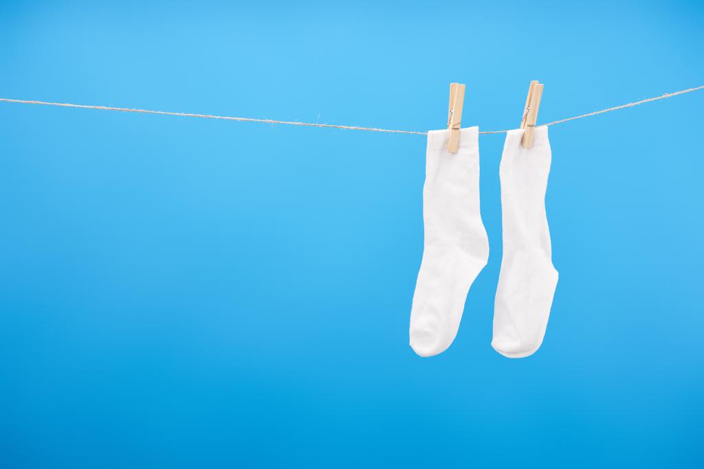крупным планом вид чистых белых носков, висящих на веревке, изолированных на голубом
  - Фото, изображение