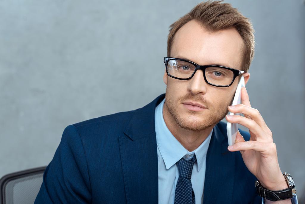 portrét pohledný podnikatel v brýlích mluví na smartphone a při pohledu na fotoaparát v úřadu  - Fotografie, Obrázek