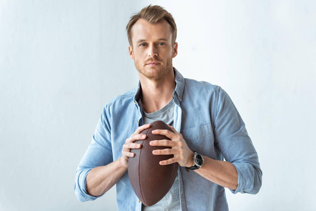 confident handsome man holding rugby ball and looking at camera near wall  - Photo, Image