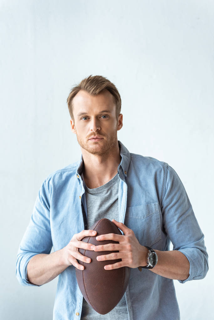young serious man holding rugby ball and looking at camera near wall  - Photo, Image