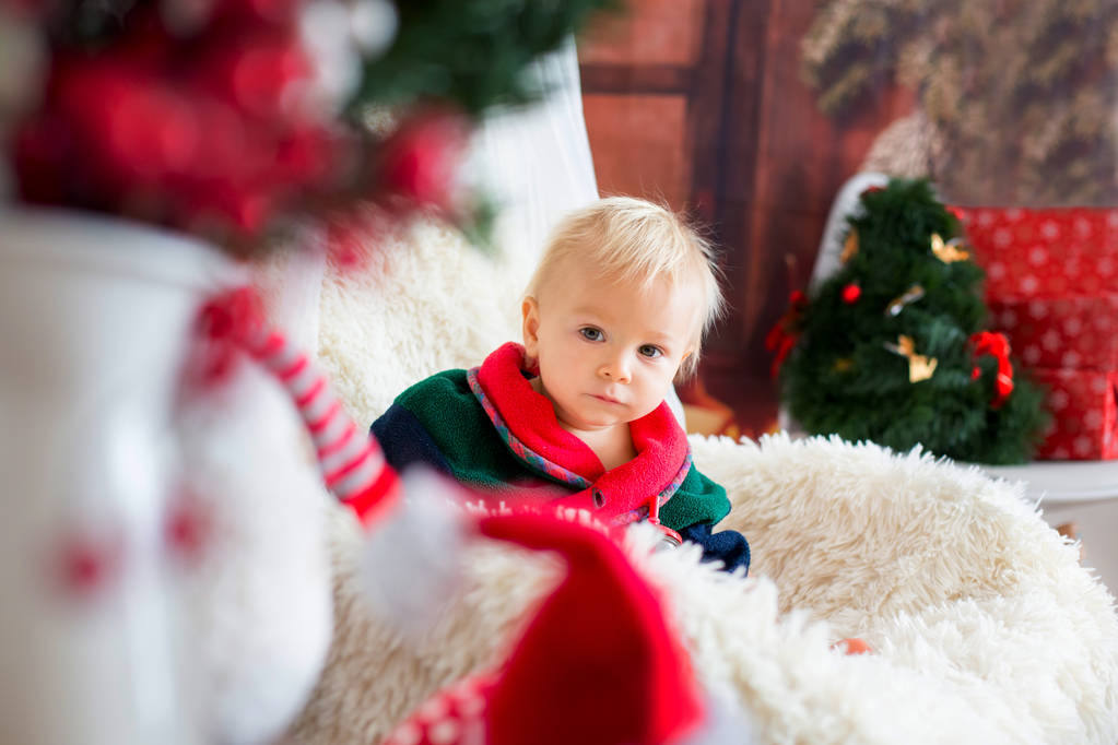 Baby Boy, niedliches Kind, in Weihnachtsmannmantel im Schaukelstuhl sitzend mit Weihnachtsbaum und Lichtern im Hintergrund im Zimmer, schlafend, Plätzchen essendend. Frohe Weihnachten. Ferienzeit. - Foto, Bild