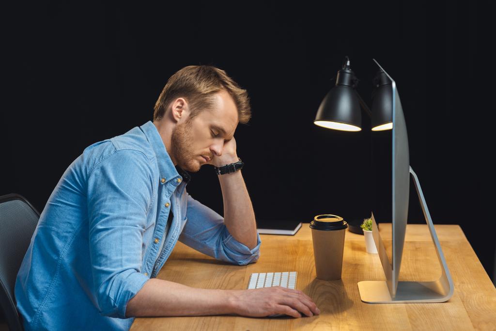 オフィスで夜の時間中にコンピューターと紙のコーヒー カップのテーブルで寝ている実業家の側面図  - 写真・画像