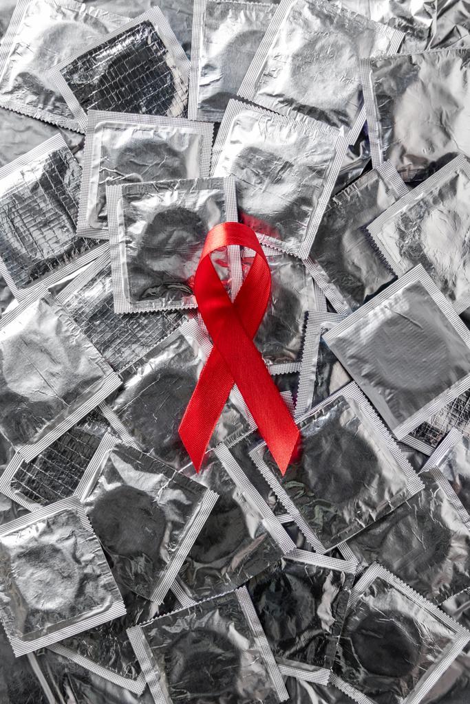 Blick von oben auf Hilfsmittel Bewusstsein rote Schleife auf silbernen Kondomen  - Foto, Bild