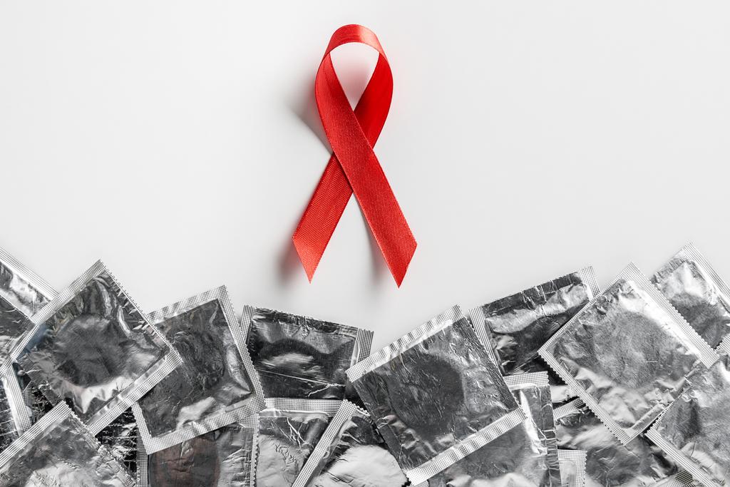 κάτοψη του aids ευαισθητοποίησης κόκκινη κορδέλα και ασημένια προφυλακτικά σε άσπρο φόντο, ιατρική έννοια - Φωτογραφία, εικόνα