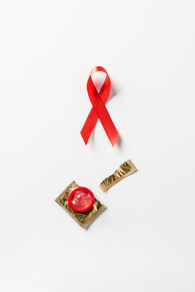 Aufsicht über Hilfsmittel Bewusstsein rote Schleife und rotes Kondom mit goldener Verpackung auf weißem Hintergrund - Foto, Bild