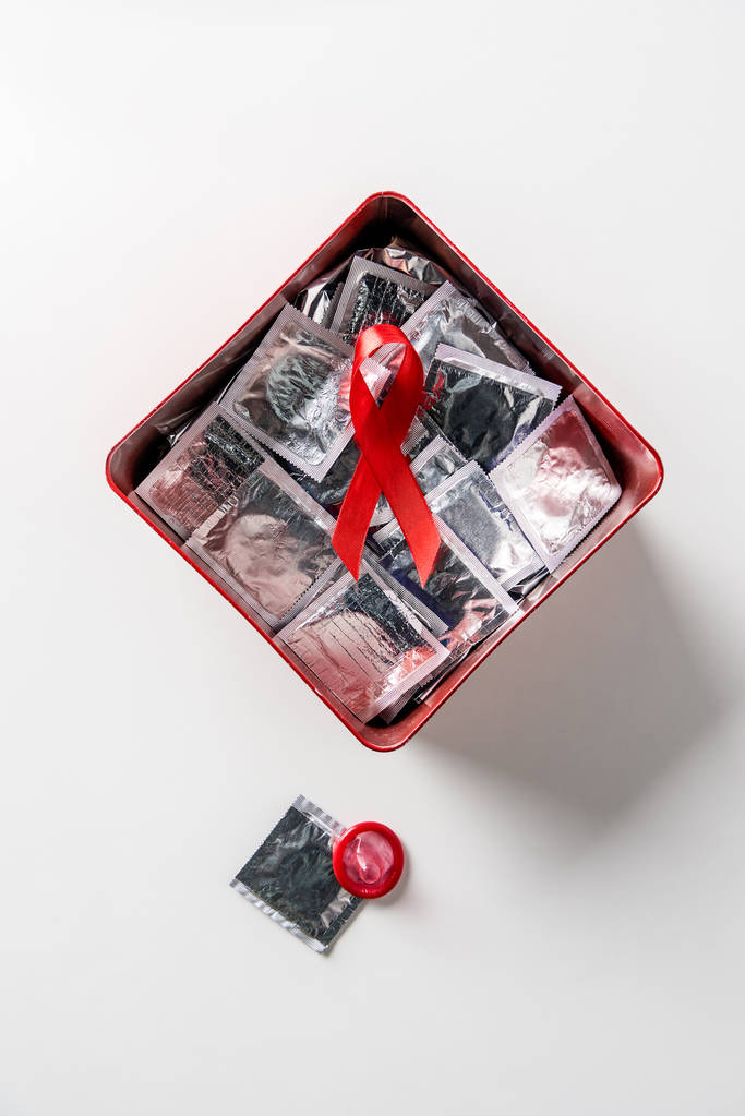 Draufsicht auf Hilfsmittel Bewusstsein rotes Band und silberne Kondome in roter Schachtel auf weißem Hintergrund - Foto, Bild