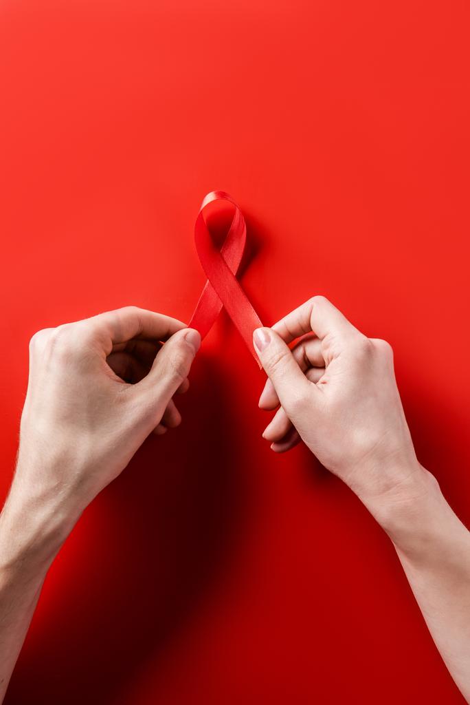 vrouwelijke handen met aids bewustzijn rood lint op rode achtergrond - Foto, afbeelding