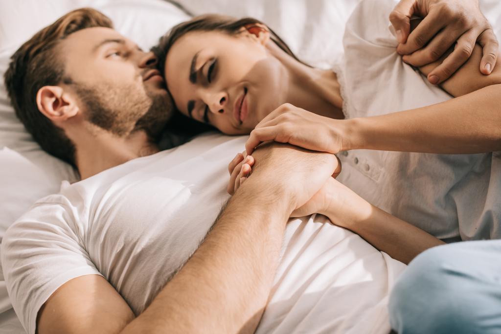 bella giovane coppia in pigiama che si tiene per mano a letto al mattino
 - Foto, immagini