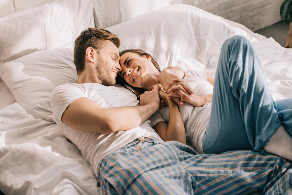 朝のベッドで抱きしめるパジャマで美しい若いカップル - 写真・画像