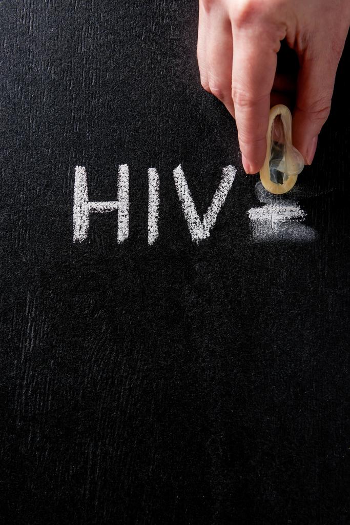 Frauenhand hält Kondom mit Hiv-Zeichen auf schwarzem Hintergrund - Foto, Bild