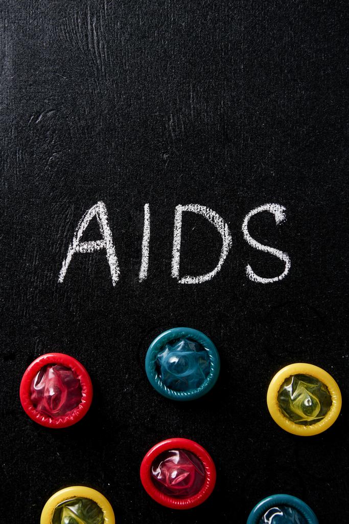 top view of aids sign with multicolored condoms on black background - Photo, Image
