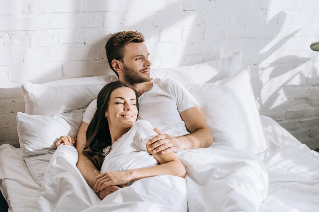 hansdome jonge man ontspannen in bed met zijn slapende vriendin in ochtend - Foto, afbeelding