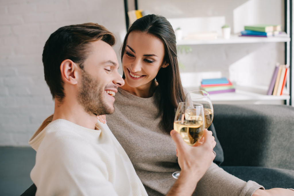 自宅のソファでワインを飲みながら美しい若いカップル - 写真・画像