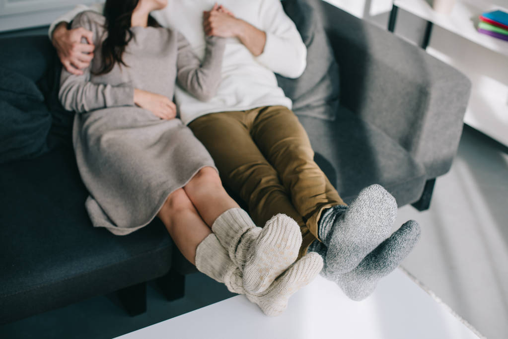 περικοπεί shot από ζευγάρι σε ζεστά μάλλινα κάλτσες χαλαρώνοντας στον καναπέ στο σπίτι - Φωτογραφία, εικόνα