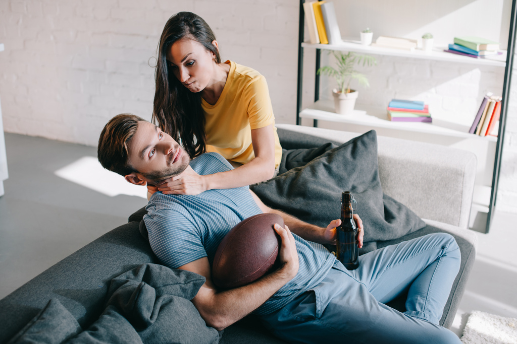 boze vrouw verstikking van haar echtgenoot terwijl hij Amerikaans voetbal kijken op tv thuis - Foto, afbeelding