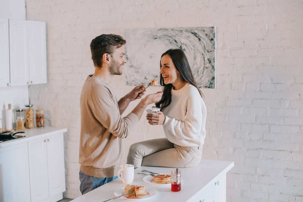 счастливый молодой человек кормит свою девушку блинчиками на завтрак
 - Фото, изображение