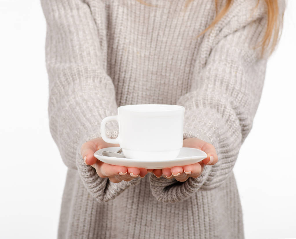 Giovane donna in maglione in possesso di una tazza bianca e piattino in mano, bere caffè caldo
. - Foto, immagini