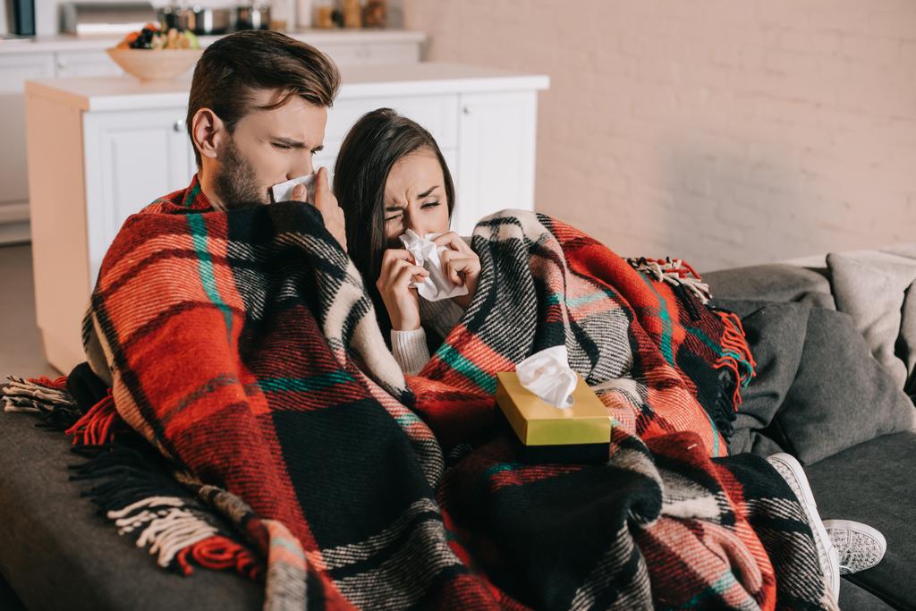 malade jeune couple avec serviettes en papier éternuer tout en étant assis sur le canapé sous plaid à la maison
 - Photo, image