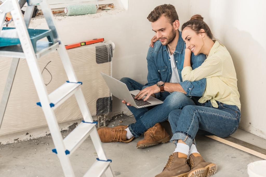 высокий угол обзора молодой пары с помощью ноутбука, сидя на полу в новом доме
  - Фото, изображение