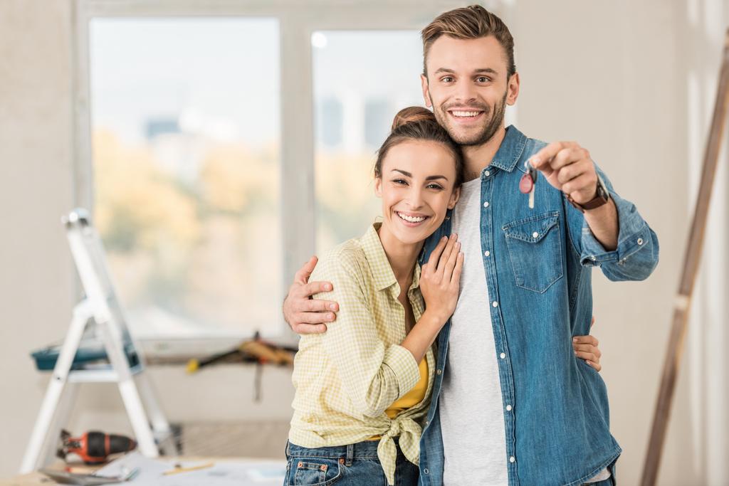 счастливая молодая пара держит ключ от новой квартиры и улыбается на камеру
 - Фото, изображение