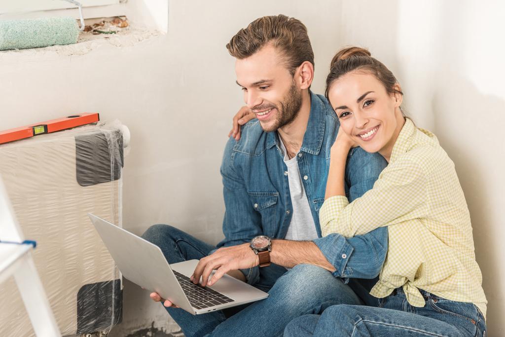 Улыбающаяся молодая пара использует ноутбук, сидя на полу в новой квартире
 - Фото, изображение
