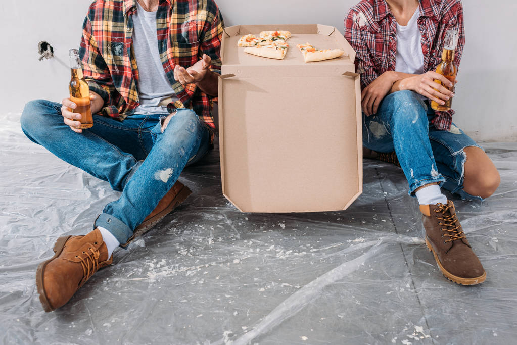 обрізаний знімок молодої пари, що тримає пляшки пива і сидить з коробкою для піци в новій квартирі
 - Фото, зображення