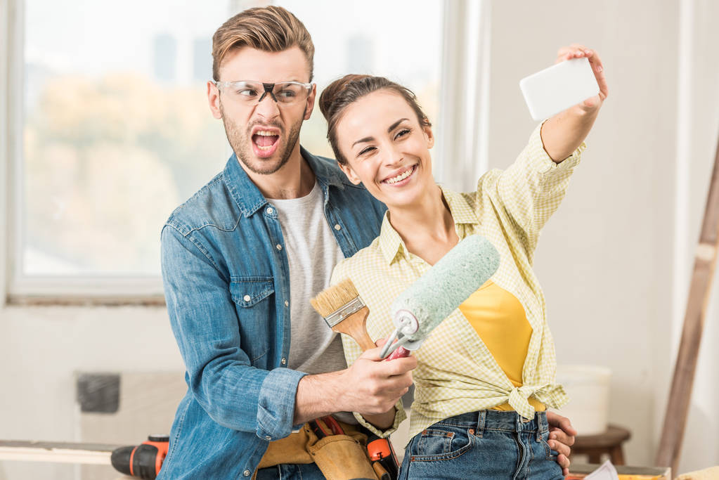 gelukkige jonge paar houden van hulpmiddelen en het nemen van selfie met smartphone tijdens renovatie - Foto, afbeelding