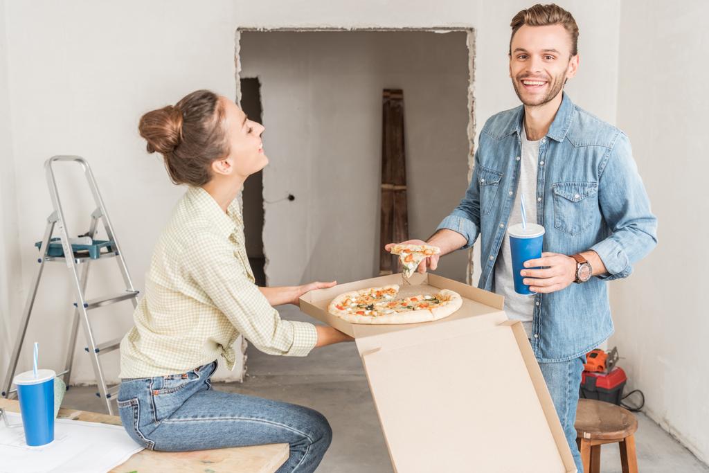 happy young couple eating pizza during repairment in new apartment - Photo, Image