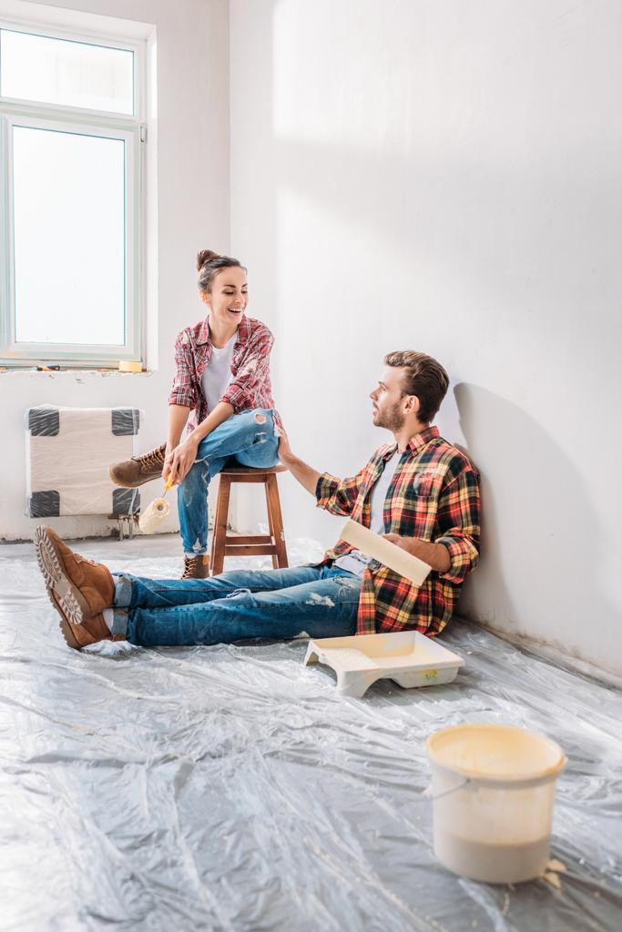 sonriente joven pareja sosteniendo rodillos de pintura y hablando en nuevo apartamento
 - Foto, imagen
