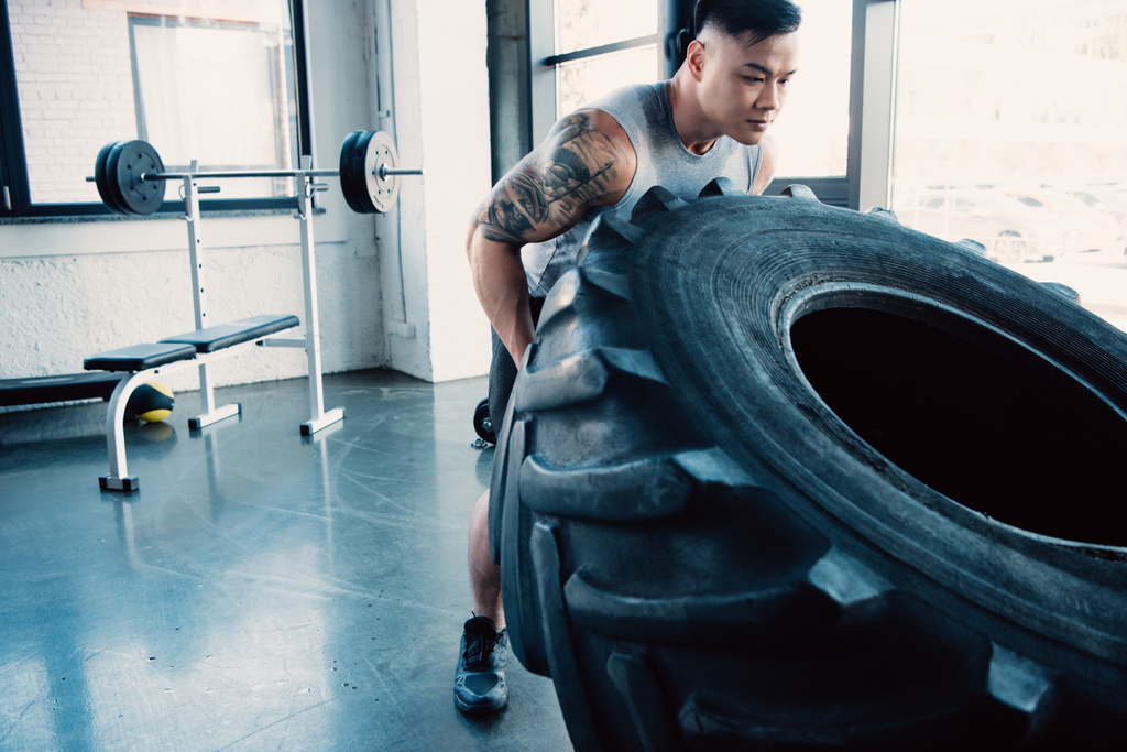 focused young sportsman flipping heavy tire at gym - Photo, Image
