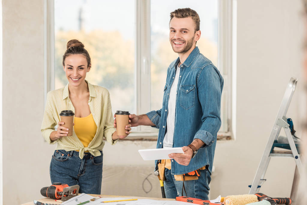 щаслива молода пара тримає паперові чашки і цифровий планшет під час ремонту в новій квартирі
 - Фото, зображення