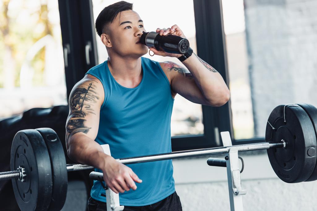 musculoso asiático deportista beber agua y entrenamiento con barbell en gimnasio
 - Foto, Imagen