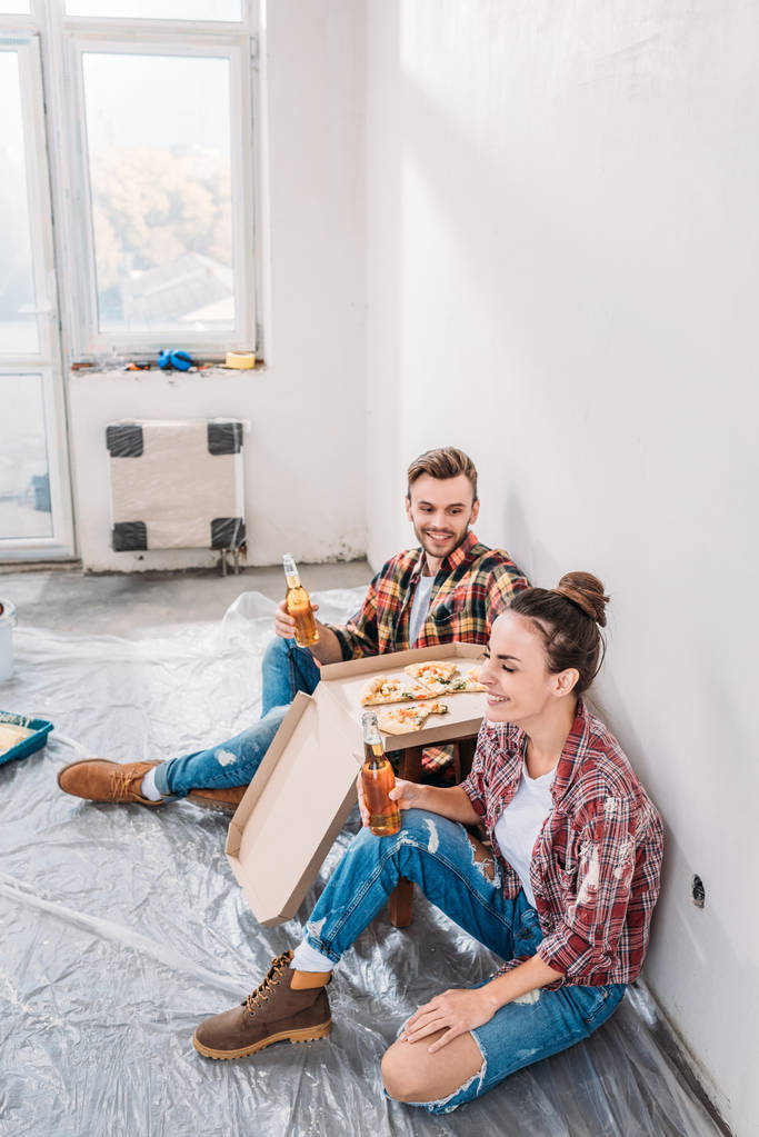 vista de ángulo alto de feliz pareja joven beber cerveza y comer pizza durante la mejora del hogar
 - Foto, Imagen