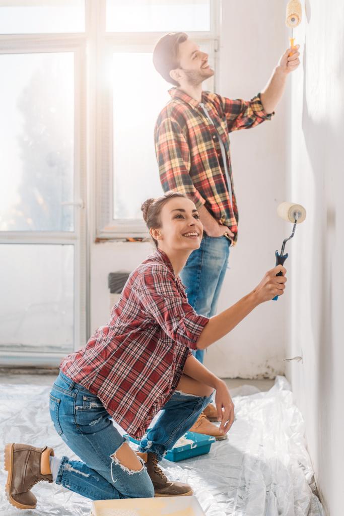 happy young couple painting wall with paint rollers in new apartment - Photo, Image