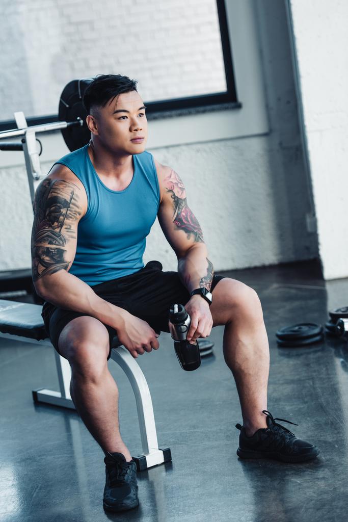 schöner junger Sportler sitzt mit Wasserflasche im Fitnessstudio - Foto, Bild