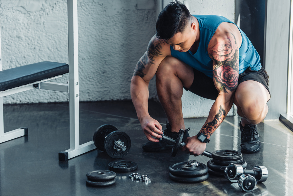 татуированный спортсмен собирает гантели в спортзале
 - Фото, изображение