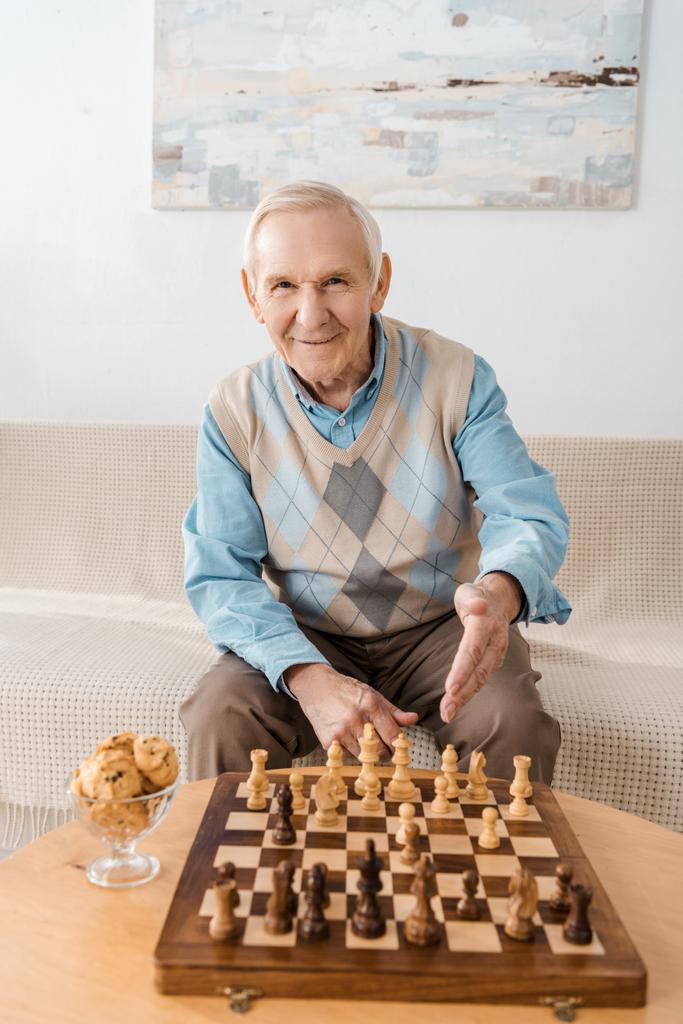 kanepede oturan ve satranç oynarken gülümseyen kıdemli adam - Fotoğraf, Görsel