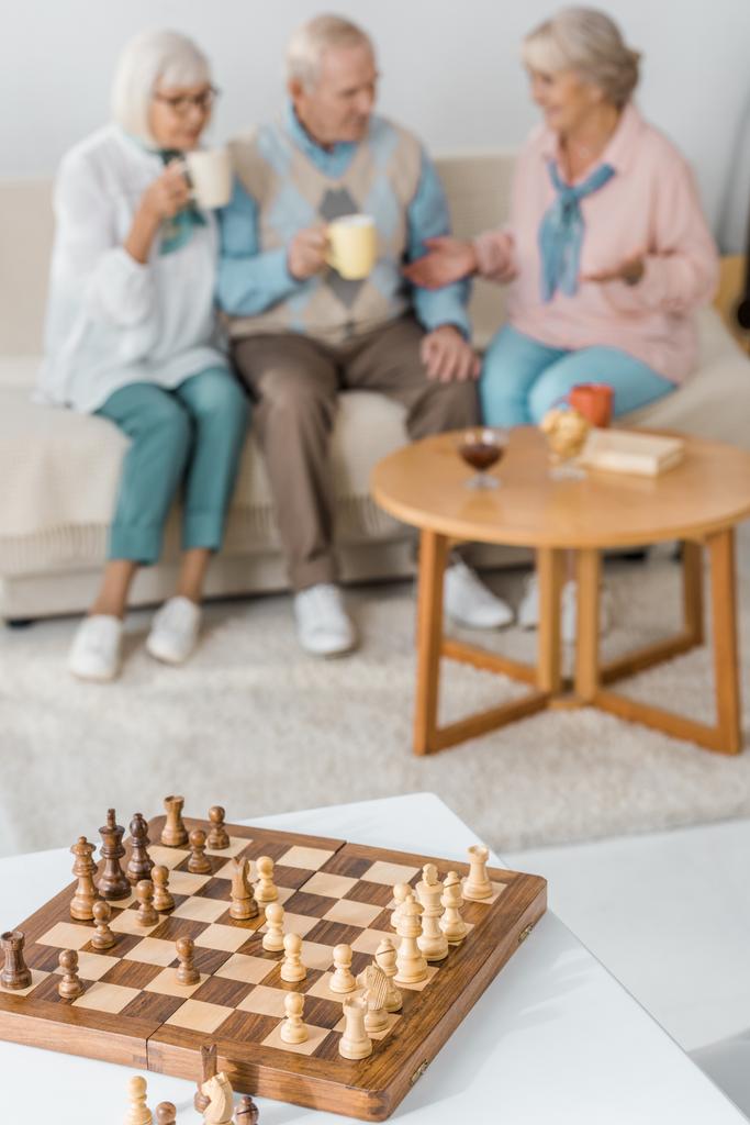 dřevěné šachy stůl s postavami a rozmazané starších lidí na pozadí - Fotografie, Obrázek