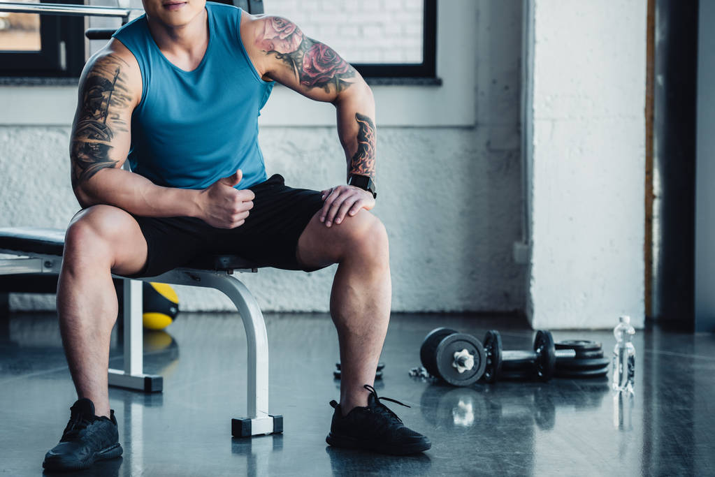 recortado vista de muscular joven deportista sentado en el gimnasio
  - Foto, Imagen