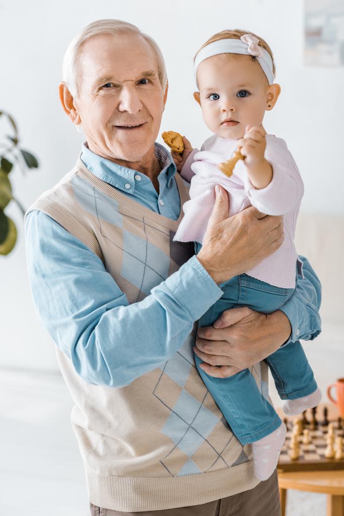 ανώτερος ο παππούς κρατώντας toddler εγγονή με μπισκότο και σκάκι φιγούρα στα χέρια - Φωτογραφία, εικόνα