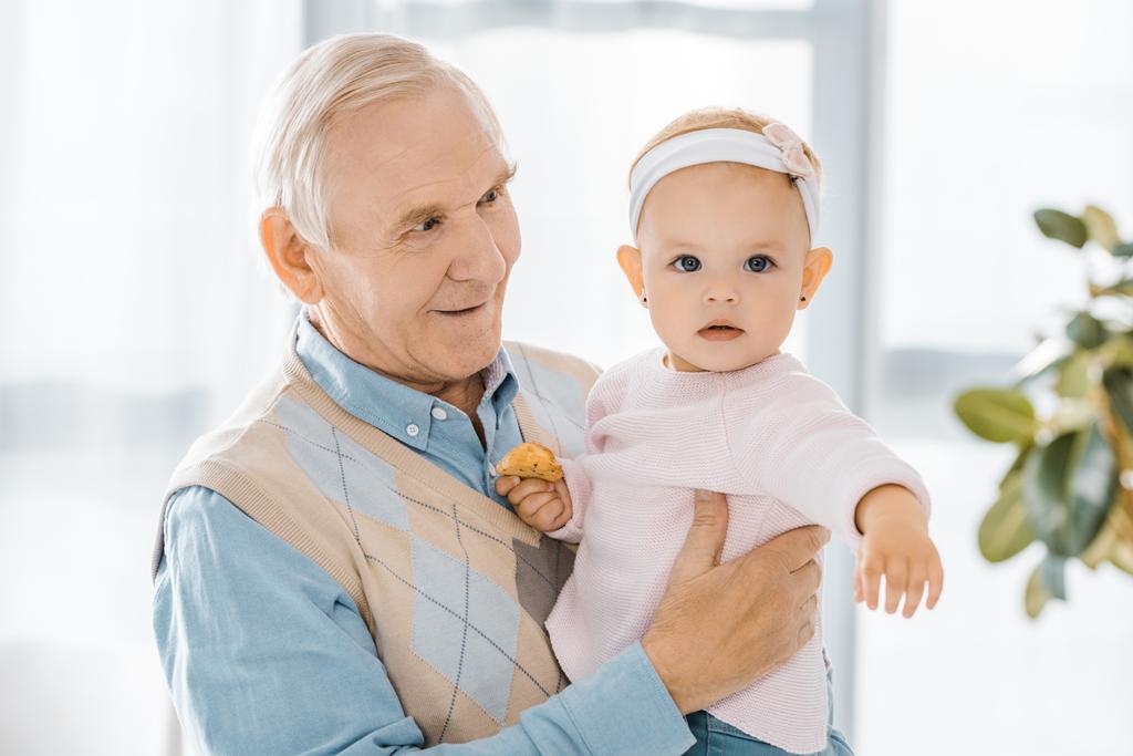 sênior sorrindo avô segurando criança neta com biscoito
 - Foto, Imagem