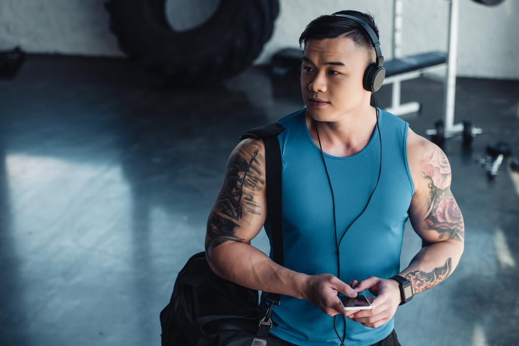 jeune sportif asiatique en utilisant smartphone et écouter de la musique dans la salle de gym
 - Photo, image
