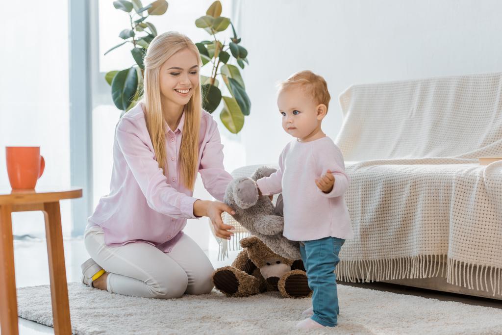 mujer joven con hija pequeña jugando juguetes en la alfombra
 - Foto, imagen