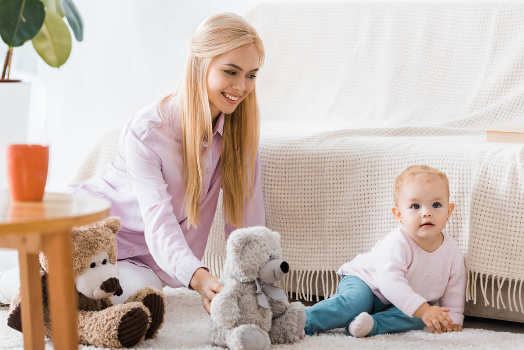 jonge vrouw met schattige dochter spelen speelgoed op tapijt - Foto, afbeelding