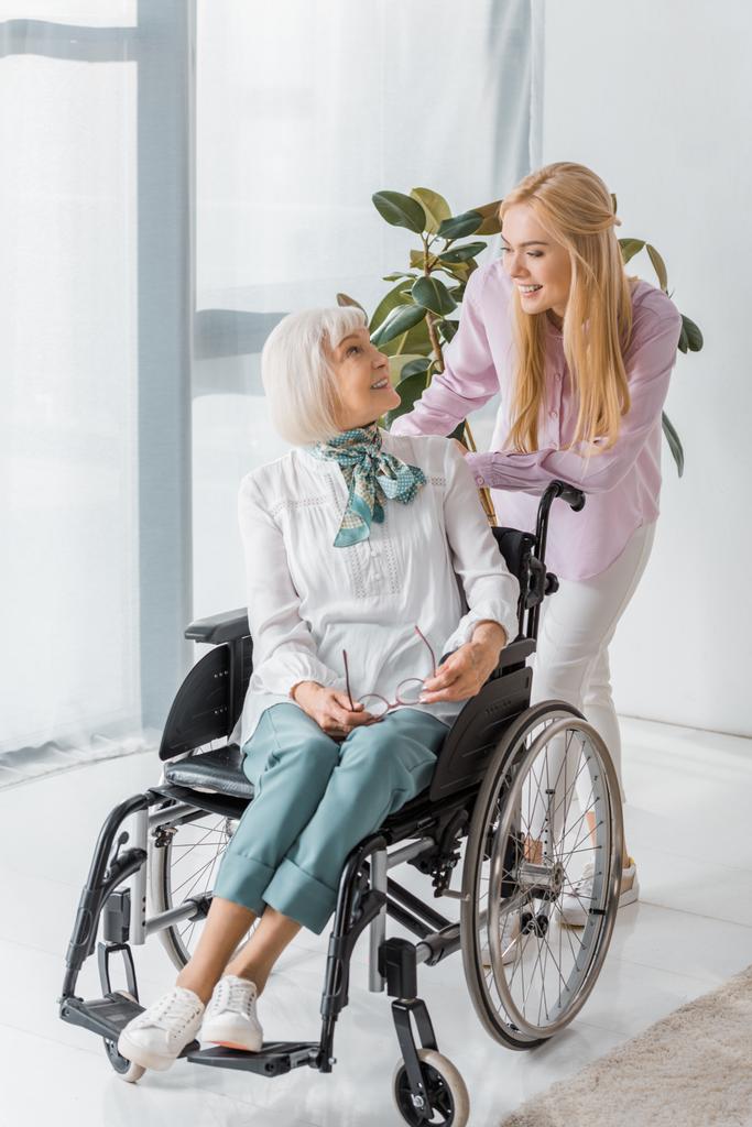 Nuori nainen puhuu vanhemman naisen kanssa pyörätuolissa hoitokodissa
 - Valokuva, kuva